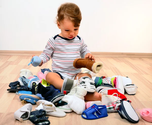 Peuter spelen met een heleboel baby schoenen. — Stockfoto