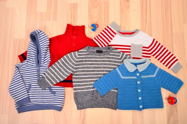 Baby clothes lying on the floor. Winter child sweaters arranged. — Stock Photo, Image