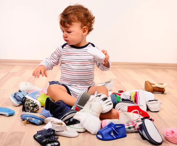 Niño jugando con un montón de zapatos de bebé . Imagen de stock