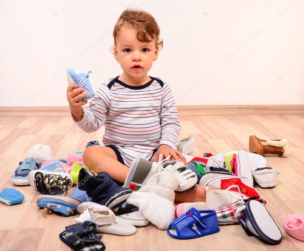 Toddler playing with a lot of baby shoes holding one shoe up.