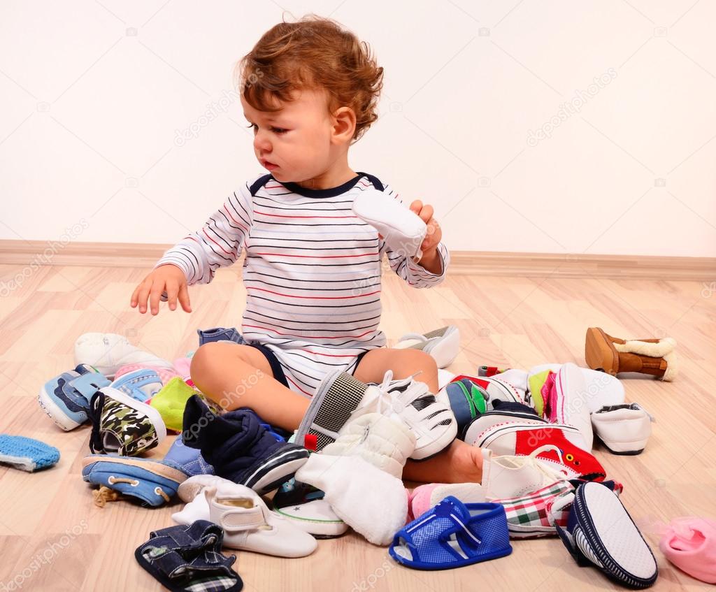 Toddler playing with a lot of baby shoes.