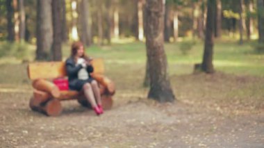Kırmızı çizmeli kahverengi saçlı ve sonbaharda parktaki bankta kırmızı çantalı bir kadın telefonla konuşuyor.