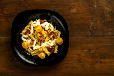 Tahta bir masada siyah tabakta tavuk ve peynirli makarna..