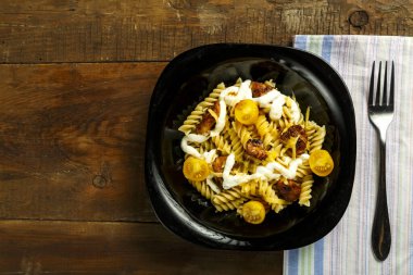 Tavuklu makarna ve peynirli siyah bir tabakta, çatallı bir peçetede..