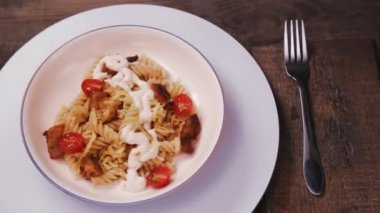 Tavuklu makarna ve domatesli makarna gri tabakta bir çatalın yanında daire şeklinde döner..