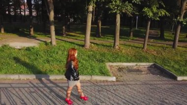 Kırmızı çizmeli, kahverengi saçlı ve kırmızı çantalı bir kadın güneşli bir günde sonbaharda bir ara sokakta yürüyor.