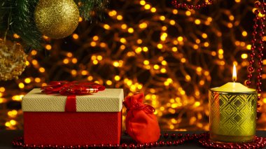 Noel ağacı dalının köşesindeki altın çelenklerin Bokeh Noel arkaplanı. Noel ağacı kutularının altında parlak bir top ve içinde hediye ve mum olan bir çanta..