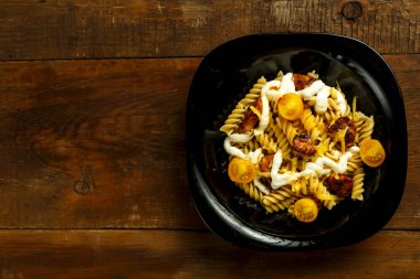 Tahta bir masada siyah tabakta tavuk ve peynirli makarna..