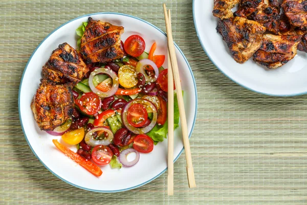 Platter of Pan-Asian sesame salad and grilled chicken pieces in Pad Thai sauce on a bamboo tablecloth.