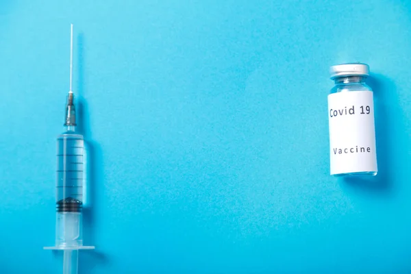 Op een blauwe achtergrond, een spuit en een injectieflacon met coronavirusvaccin. — Stockfoto