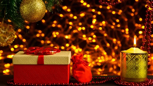 Noel ağacı dalının köşesindeki altın çelenklerin Bokeh Noel arkaplanı. Noel ağacı kutularının altında parlak bir top ve içinde hediye ve mum olan bir çanta..