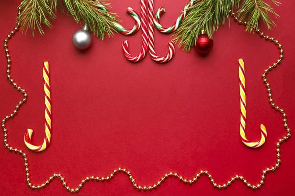 Cadre de Noël avec des bonbons de couleur sucre et des branches de pin avec des décorations ibus sur un fond rouge lieu pour une inscription. — Photo