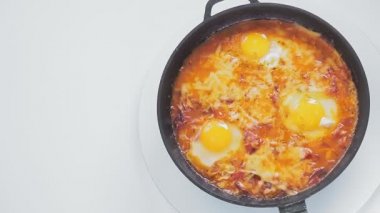 Shakshuka ve peynirli tava beyaz arka planda daire şeklinde döner.