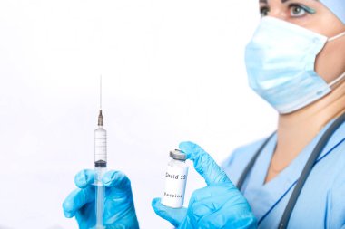 Virüse karşı aşısı olan bir şişe ve maskeli bir doktorun elinde şırınga..