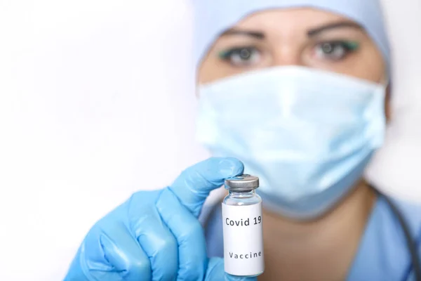 Een injectieflacon met een vaccin tegen het virus in de handen van een gemaskerde arts. — Stockfoto