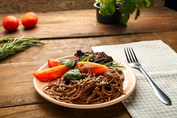 Ein Teller Soba mit Huhn, Tomaten und Spinat auf einer Leinenserviette neben einer Gabel auf dem Tisch mit Gemüse. — Stockfoto