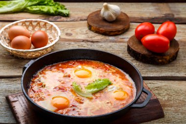 İsrail usulü yağda yumurtalı shakshuka ve peynirli kızartma tavası masada ürünlerin yanında..