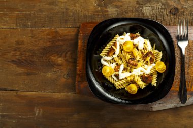 Tavuklu makarna ve peynirli siyah bir tabak içinde ahşap bir tezgahta çatalla..