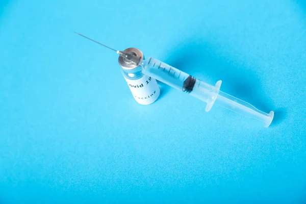 Op een blauwe achtergrond, een spuit en een injectieflacon met coronavirusvaccin, bovenaanzicht. — Stockfoto