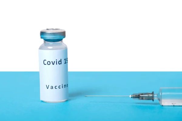 青いテーブルの上には注射器とコロナウイルスワクチンの瓶があります. — ストック写真