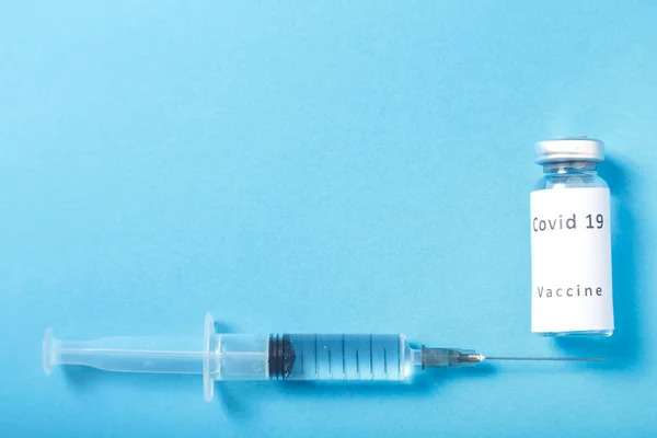 Op een blauwe achtergrond, een spuit en een injectieflacon met een vaccin tegen het virus. — Stockfoto