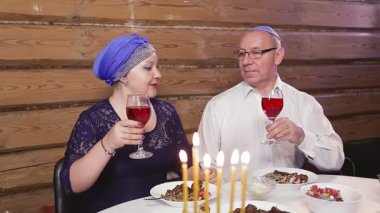 Yahudi evli bir çift başlıklı bir eş bayram masasında kippah giymiş bir adam ve Hanuka günlerinde yanan mumlar.