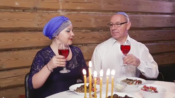 Judío casado pareja una esposa en un tocado un hombre en un kippah en una mesa festiva con velas encendidas en los días de Hanukkah — Vídeo de stock