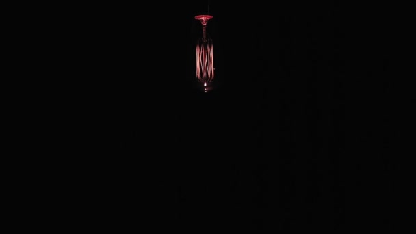 Une lampe à incandescence en bobine de tungstène suspendue au sommet s'allume et s'éteint sur un fond noir. Espace de copie. — Video