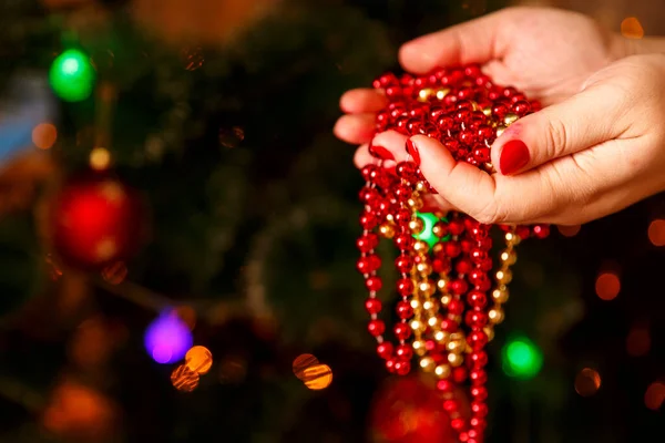 Weihnachtsschmuck einer Kette in weiblichen Händen auf dem Hintergrund eines Weihnachtsbaums. — Stockfoto