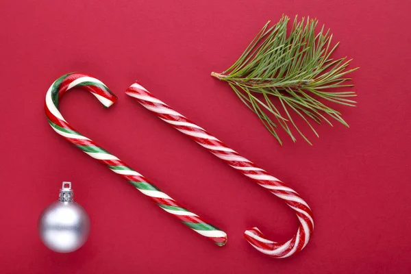 Natale sfondo rosso con un rametto di pino, un albero di Natale cono giocattolo e lecca-lecca. — Foto Stock