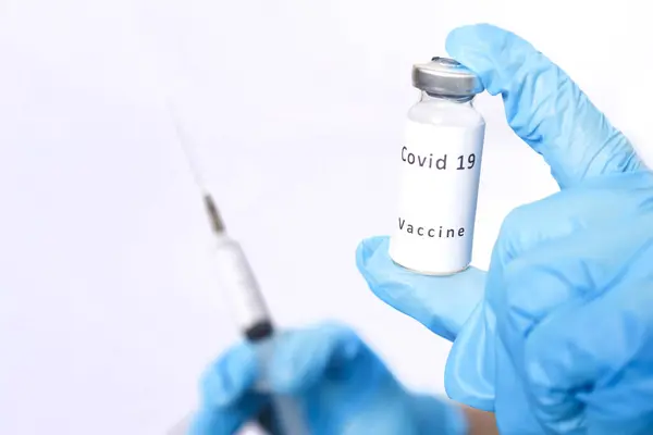Een injectieflacon met een vaccin tegen het virus en een spuit in de handen van een gemaskerde arts. — Stockfoto