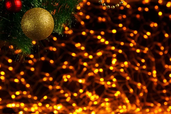 Bokeh Weihnachten Neujahr Hintergrund aus goldenen Girlanden auf schwarz in der Ecke eines Weihnachtsbaumzweiges mit einer Kugel. — Stockfoto