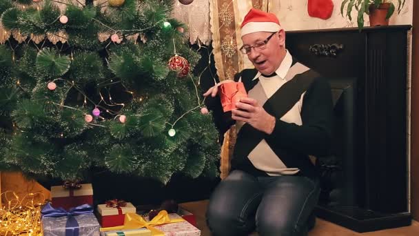 Egy férfi karácsonykor a karácsonyfánál megvizsgálja az ajándékokat.. — Stock videók