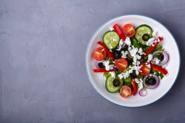 Beyaz tabak, gri beton arka planda Yunan salatası. Boşluğu kopyala.