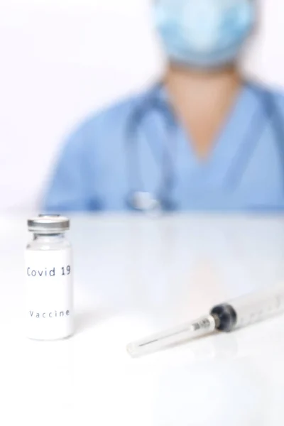 На столі лежить вакцина для профілактики вірусу і шприц на задньому плані лікар в розмитому стані . — стокове фото
