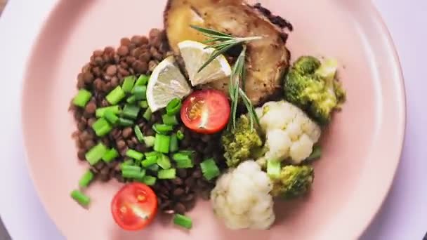 Gebakken vis met linzen en broccoli en rozemarijn op een beige plaat op een statief draait in een cirkel — Stockvideo