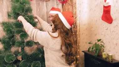 Noel Baba şapkalı bir karı koca Noel ağacını elektrik lambalarıyla süslüyor. Ortam planı