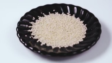 Beyaz zemin üzerinde siyah bir tabakta susam tohumları daire şeklinde döner. Ortam planı