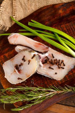 Biberiye ve soğanın yanına baharat serpiştirilmiş ahşap bir tahtada taze balık biftekleri. Dikey fotoğraf