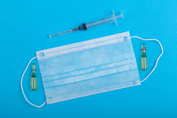 Ampoules with medicine, syringe and medical mask on a blue background. Horizontal photo
