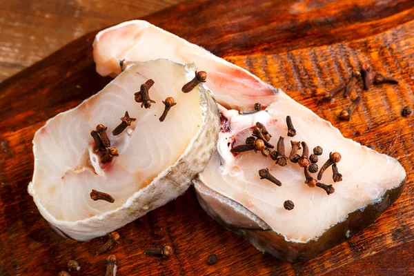 Стейки свіжої білої тріски риби на дерев'яній дошці, посипані спеціями . — стокове фото