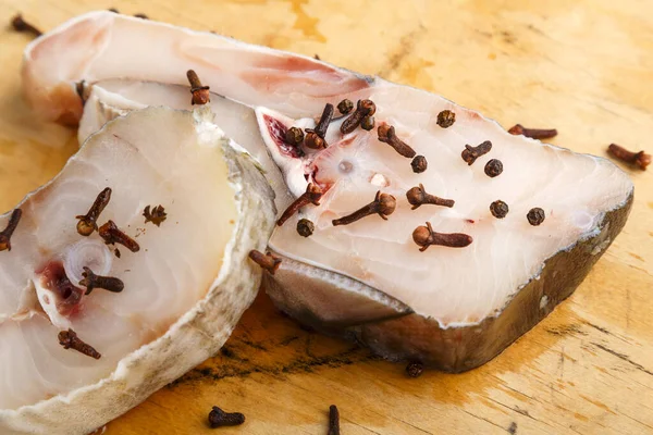 Bifes de bacalhau branco fresco em um tabuleiro polvilhado com especiarias nas proximidades. — Fotografia de Stock