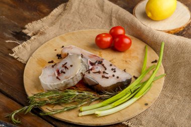 Biberiye ve soğan domateslerinin yanına baharat serpiştirilmiş yuvarlak bir tahtada taze balık biftekleri..