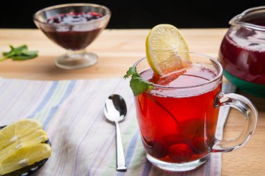 Çaydanlık kaşığının yanında bir fincanda çilek çayı ve peçetenin üstünde limon ve limon merhemi..