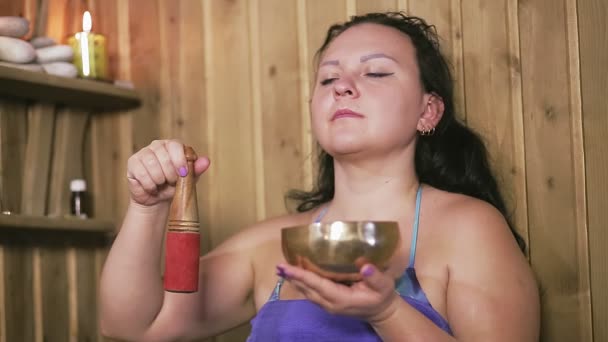 Брюнетка в полотенце в спа-салоне со свечами медитирует с чашей для пения — стоковое видео