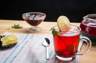 Çaydanlık kaşığının yanında bir fincanda çilek çayı ve peçetenin üstünde limon ve limon merhemi..