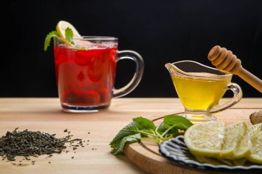 Limonun yanında bir fincanda çilek çayı, bal, limon merhemi ve masanın üzerinde bir içecek olan çaydanlık..