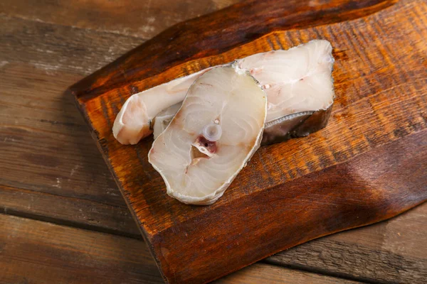 Bifes de bacalhau branco em um tabuleiro de madeira. — Fotografia de Stock