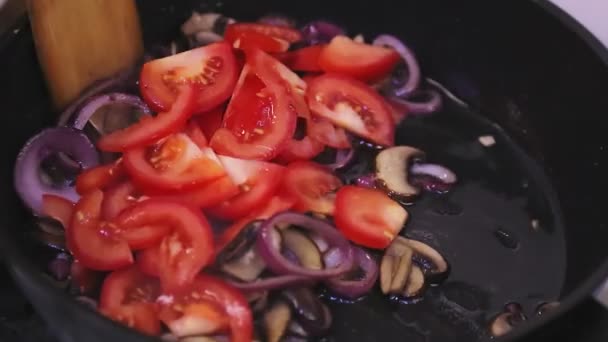 Em uma frigideira com cogumelos e cebolas, os tomates são misturados com uma espátula. — Vídeo de Stock