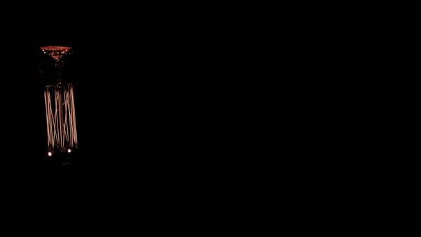 Lâmpada incandescente com uma espiral de tungstênio pendurado luzes para cima e sai em um fundo preto. Espaço de cópia — Vídeo de Stock